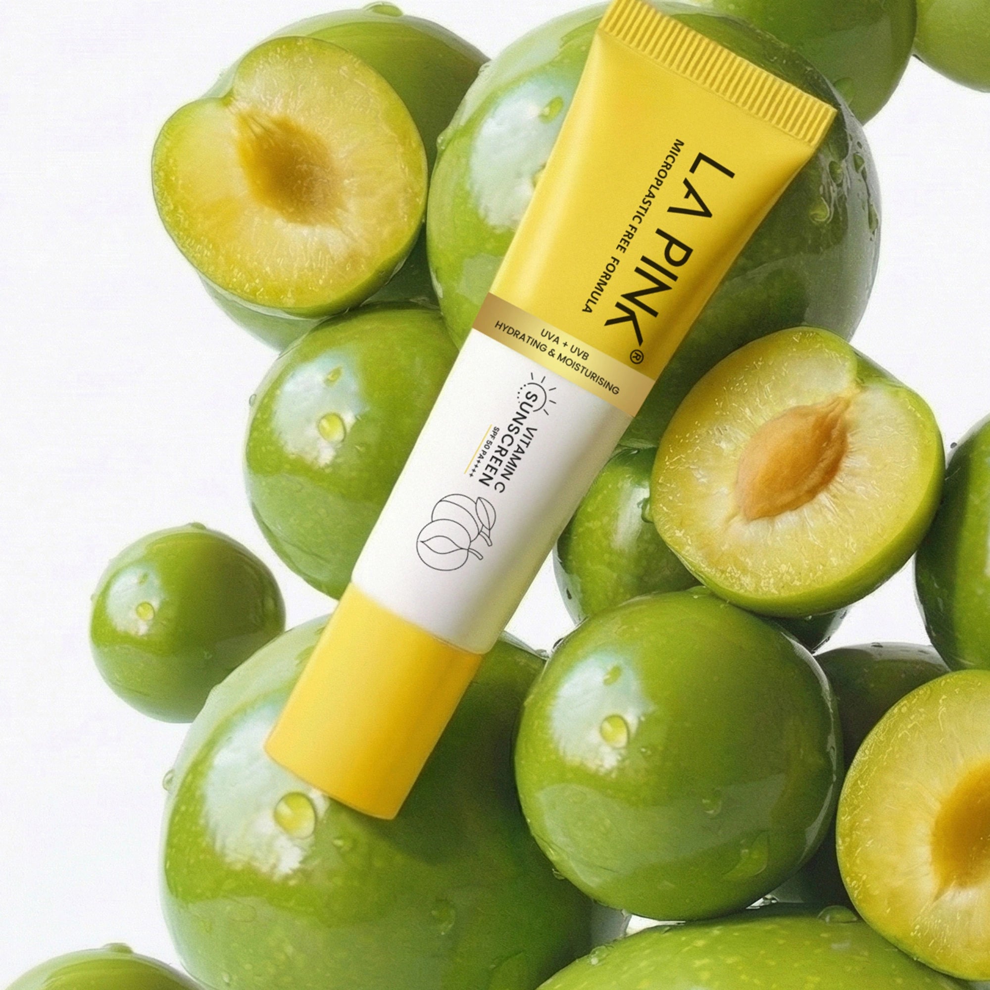 Yellow tube of LA PINK skincare product surrounded by green fruits on a white background