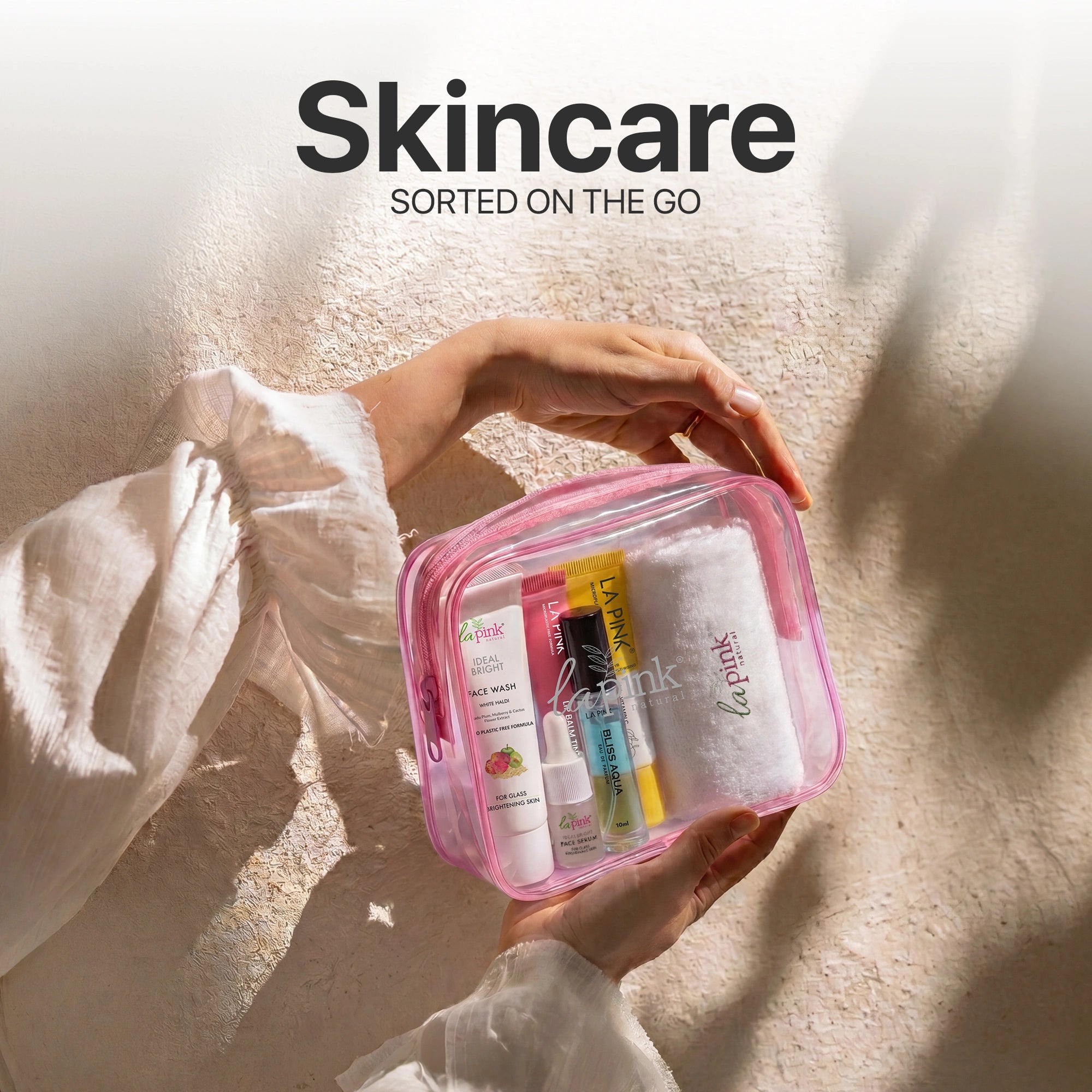 Person holding a pink skincare travel bag with products on a textured surface