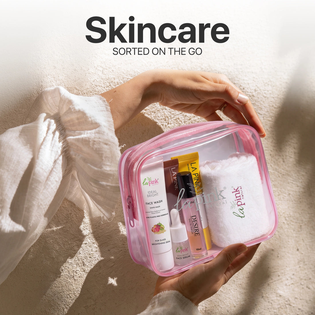 Pink skincare travel case with products held by a hand, against a neutral background.