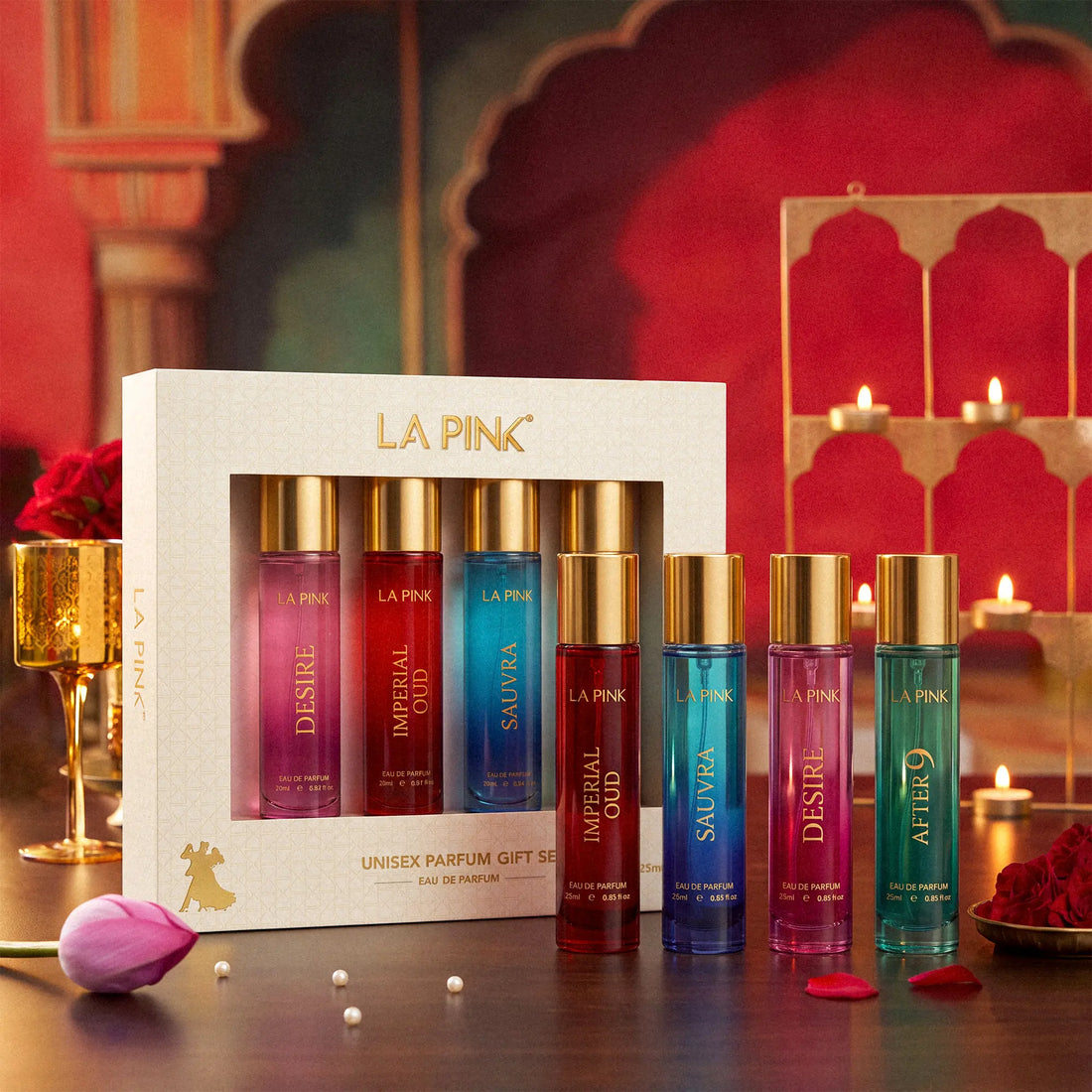 LA PINK Unisex Parfum Gift Set featuring a white box containing five 10ml travel perfume bottles with gold caps, displayed alongside five matching bottles on a dark wooden table with warm, decorative background elements.

