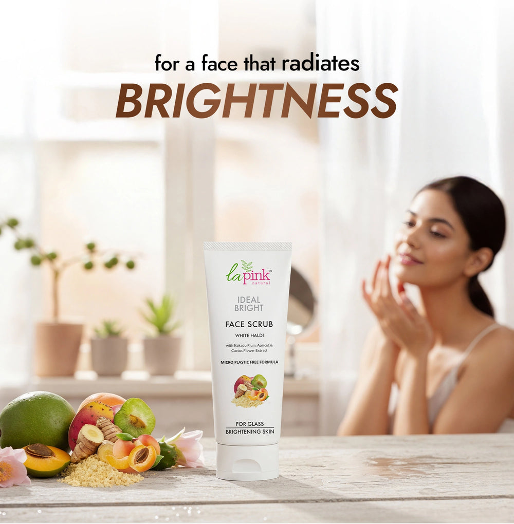 La Pink Ideal Bright Face Scrub with a woman applying cream and fruits on a table.