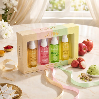 LA PINK Yum Yum Body Mist Gourmet Collection set of four body mists in a pastel-colored box, styled on a marble table with fruit, sweets, and decorative ribbons.


