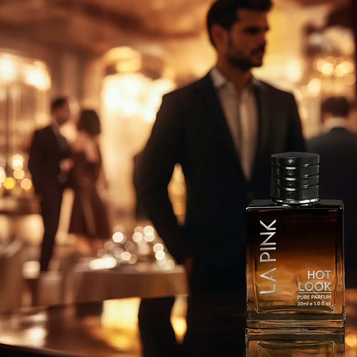 LA PINK Hot Look Pure Parfum 30ml bottle in the foreground, with a blurred man in a suit and a warm, elegant indoor event background.

