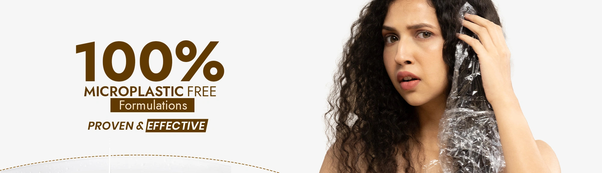 Woman with curly hair holding a bottle labeled '100% Microplastic Free Formulations' on a white background.