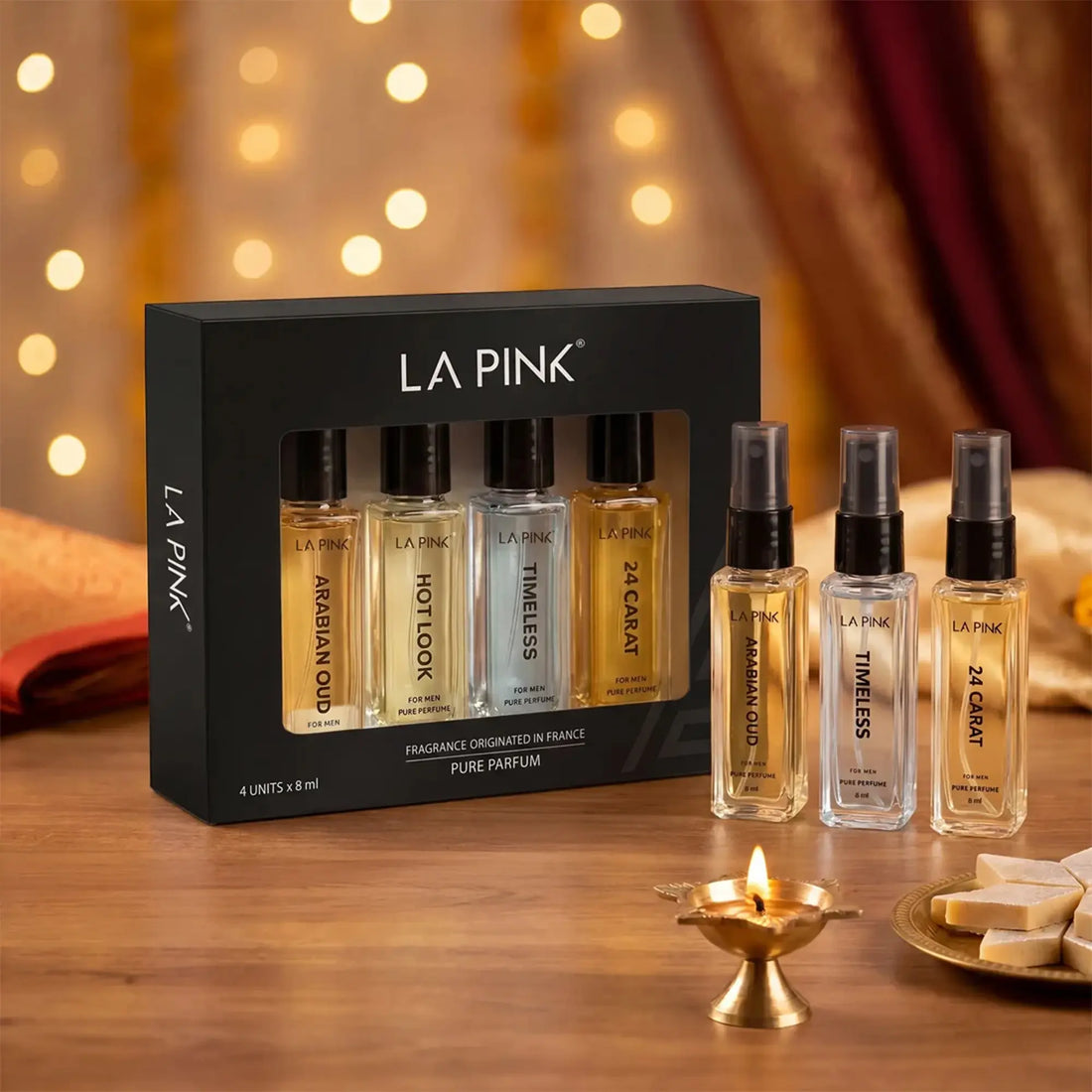 LA PINK pure perfume set with a black 4-pack box and four individual spray bottles displayed on a wooden table with warm bokeh lights in the background.

