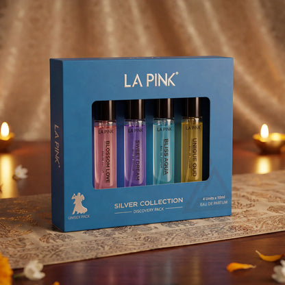 LA PINK Silver Collection 4-piece perfume discovery pack in a blue box, featuring four distinct colored bottles (pink, purple, blue, and yellow) on a patterned table runner with warm candlelit background.


