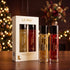 LA PINK Unisex Parfum Gift Set featuring a white box with two bottles inside and two individual bottles (Unique Oud in amber and Imperial Oud in red) on a wooden table with festive blurred lights in the background.