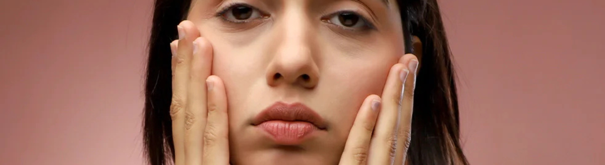 Woman with hands on face against a pink background