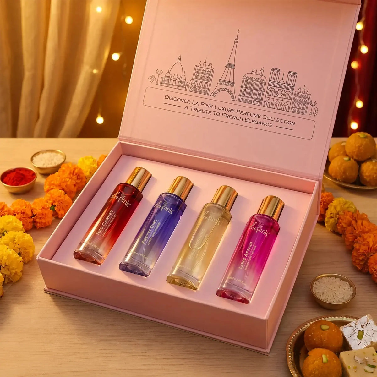 LA PINK body mist set in a colorful box with four different scents: Aqua Pell, Pure Love, Dream Romance, and Wild Secret. The set is styled on a beige surface with decorative dried flowers, pearls, and gift boxes in the background.

