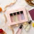 A boxed fragrance gift set from LA PINK on a white marble surface with fairy lights and ribbon. The pale pink box contains four small perfume bottles, and two additional bottles are placed outside the box.

