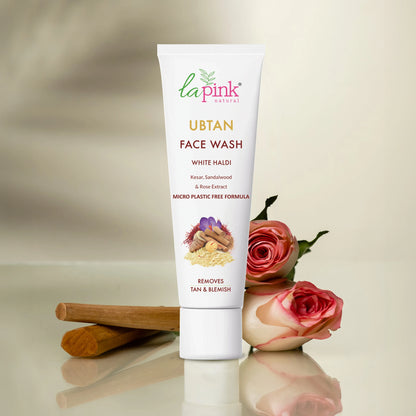 Tube of La Pink Ubtan Face Wash with roses and a cinnamon stick on a reflective surface