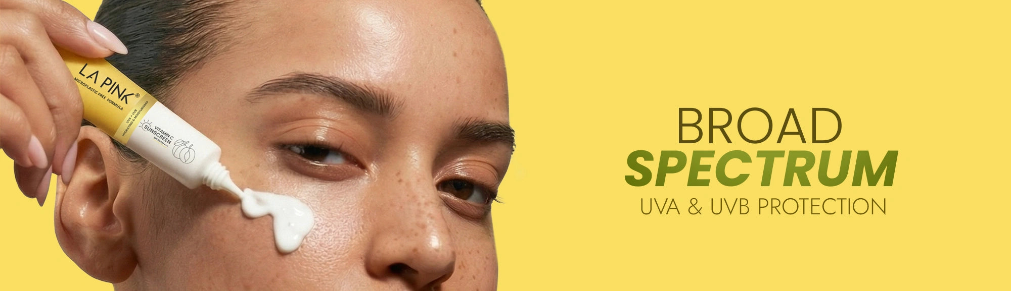Person applying sunscreen cream with 'La Pink' bottle on a yellow background, featuring 'Broad Spectrum UVA & UVB Protection' text.